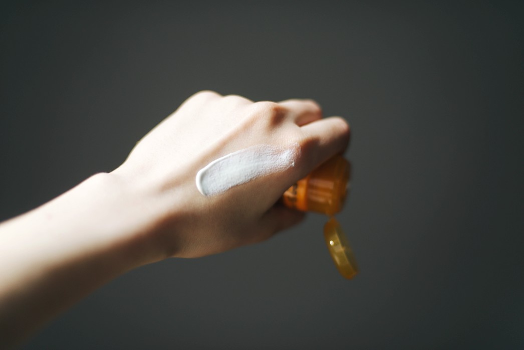 SPF sunblock hand cream on the back of a hand holding a sunscreen container