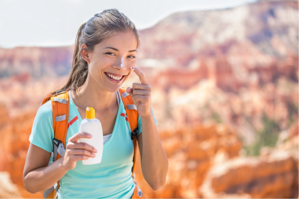 Smiling woman hiking applying sunscreen on her nose