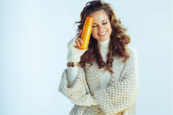 Woman in knit sweater holding sunscreen container to her forehead